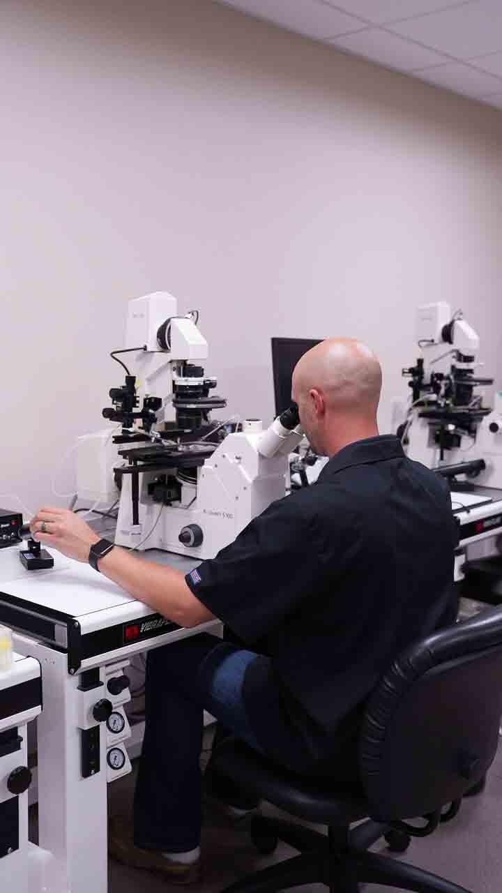 A scientist examines samples using a microscope in a lab, focusing intently on the research work at hand.