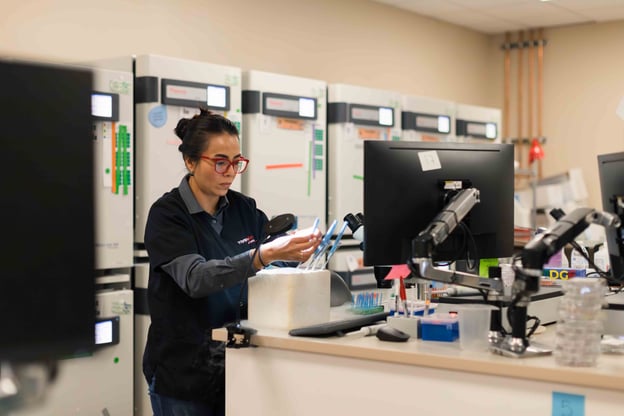 Lab technician handling samples at a workstation in a genetics laboratory.