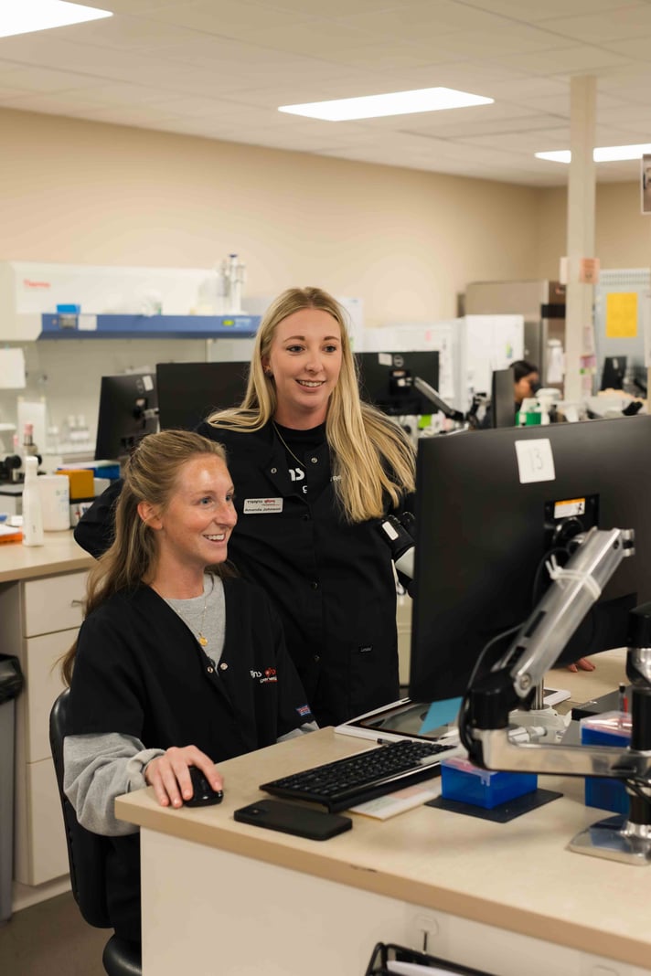 Two genetics laboratory team members reviewing information together at a computer workstation.